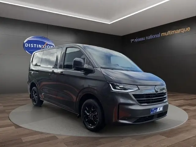 Volkswagen Transporter gris foncé en 3/4 avant droit, avec jantes noires et phares LED allumés.