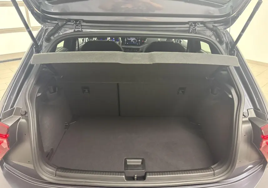Coffre ouvert vu de l'arrière d'une Volkswagen Polo gris cendré, avec plage arrière relevée et intérieur spacieux.