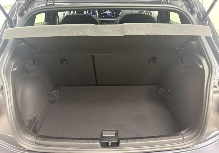 Vue arrière du coffre ouvert d'une Volkswagen Polo gris cendré, avec tablette cache-bagages relevée et intérieur spacieux visible.