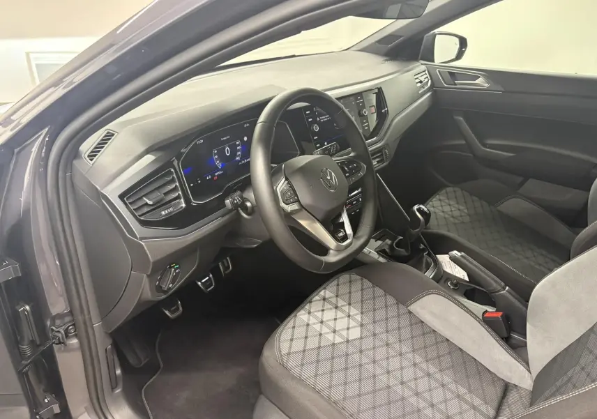 Vue intérieure côté conducteur de la Volkswagen Polo 1.0 TSI R-Line 2025 avec sièges tissu gris à motif et tableau de bord digital.