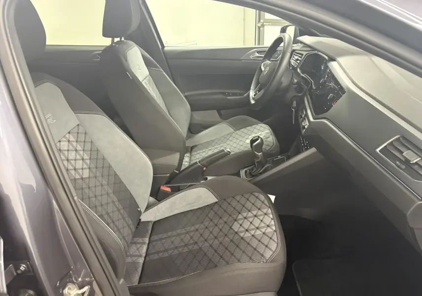 Vue intérieure côté conducteur de la Volkswagen Polo 1.0 TSI R-Line 2025 avec sièges tissu gris à motif et volant multifonction.