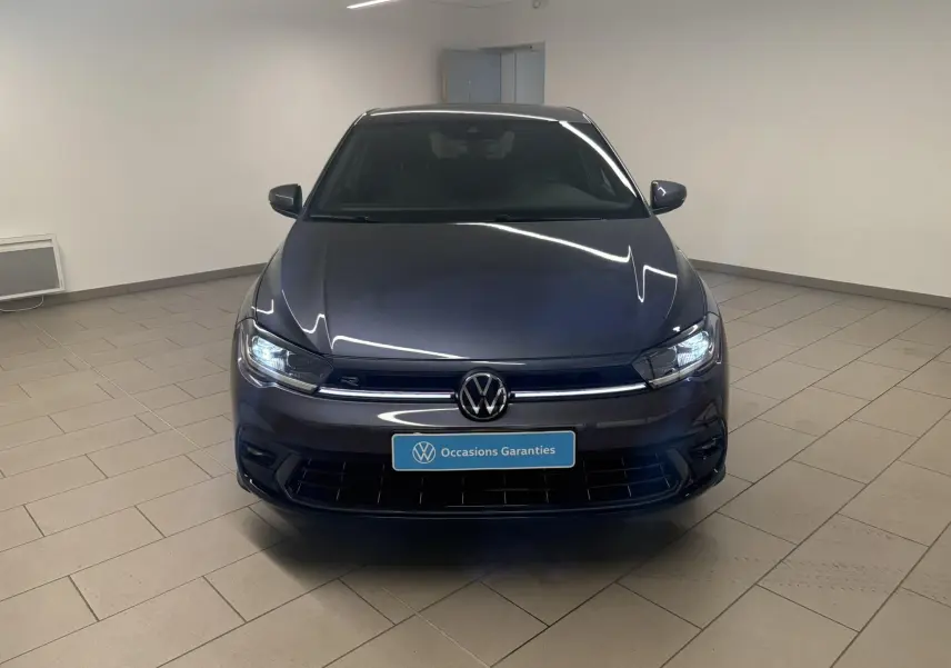Volkswagen Polo 1.0 TSI R-Line gris cendré vue de face en intérieur avec phares allumés et logo VW visible.