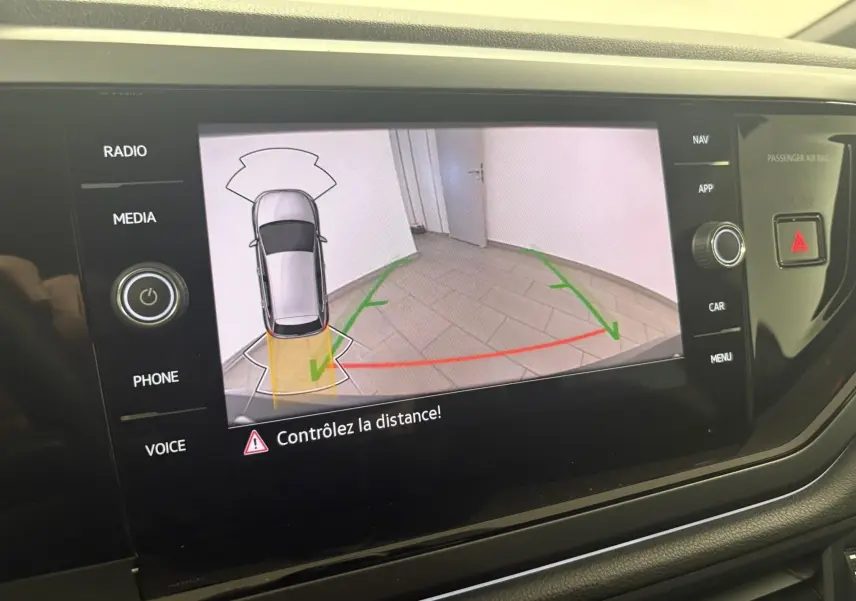 Écran de caméra de recul montrant une Volkswagen Polo gris cendré en vue aérienne avec guidage de trajectoire verte et rouge.