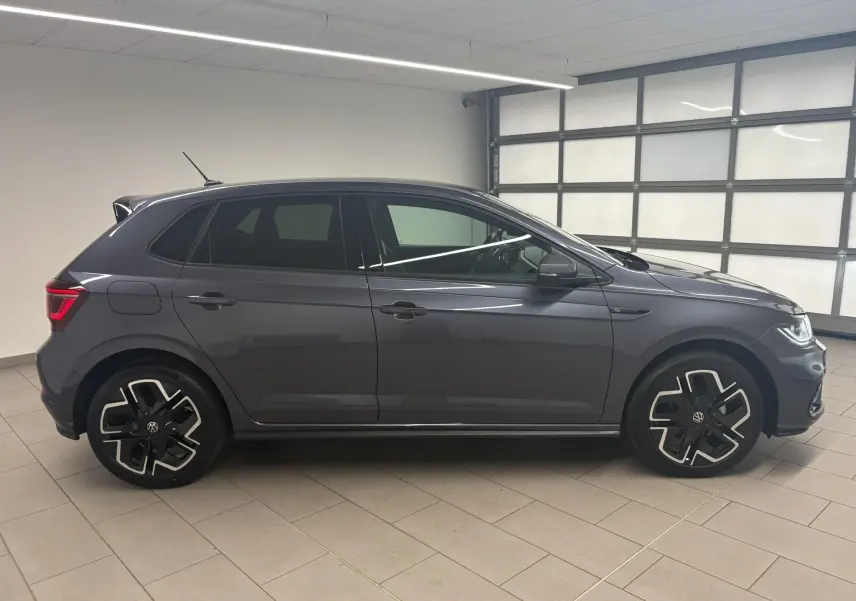 Profil droit d'une Volkswagen Polo 1.0 TSI R-Line gris cendré métallisé, avec jantes alliage distinctives, en intérieur showroom.