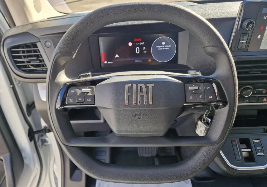 Vue intérieure centrée sur le volant noir FIAT d’un fourgon blanc avec tableau de bord numérique et commandes intégrées.