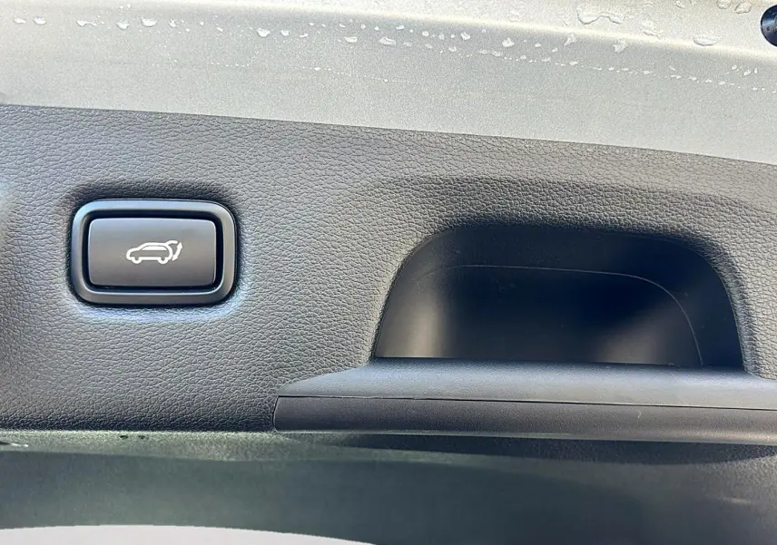 Bouton d'ouverture électrique du coffre sur la garniture intérieure noire du hayon d'un KIA Xceed gris 2024.