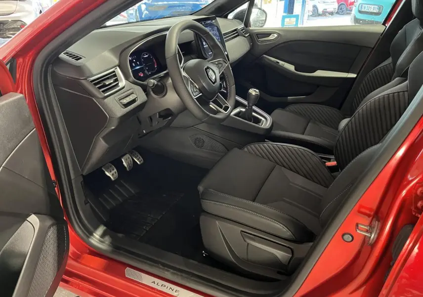 Intérieur côté conducteur de Renault Clio 2024 rouge, volant multifonction, sièges tissu noir avec surpiqûres Alpine.