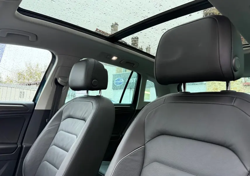Vue intérieure du Volkswagen Tiguan 2022 montrant les sièges avant en cuir noir et le toit panoramique avec pluie visible.
