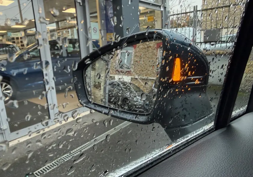 Rétroviseur côté droit du Volkswagen Tiguan bleu Night Shade avec clignotant orange sous la pluie.
