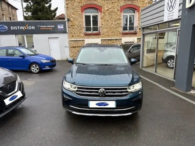 Vue frontale d'un Volkswagen Tiguan 2022 bleu Night Shade, garé devant un bâtiment en pierre sous la pluie.