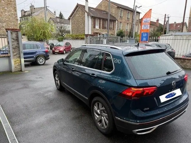 Volkswagen Tiguan 2022 bleu Night Shade, vue 3/4 arrière droit, avec feux arrière allumés et toit ouvrant fermé.