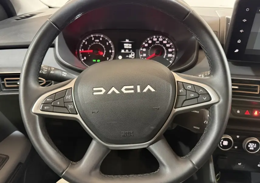 Vue rapprochée du volant en cuir synthétique noir de la Dacia Sandero 2024 avec commandes multifonctions visibles.