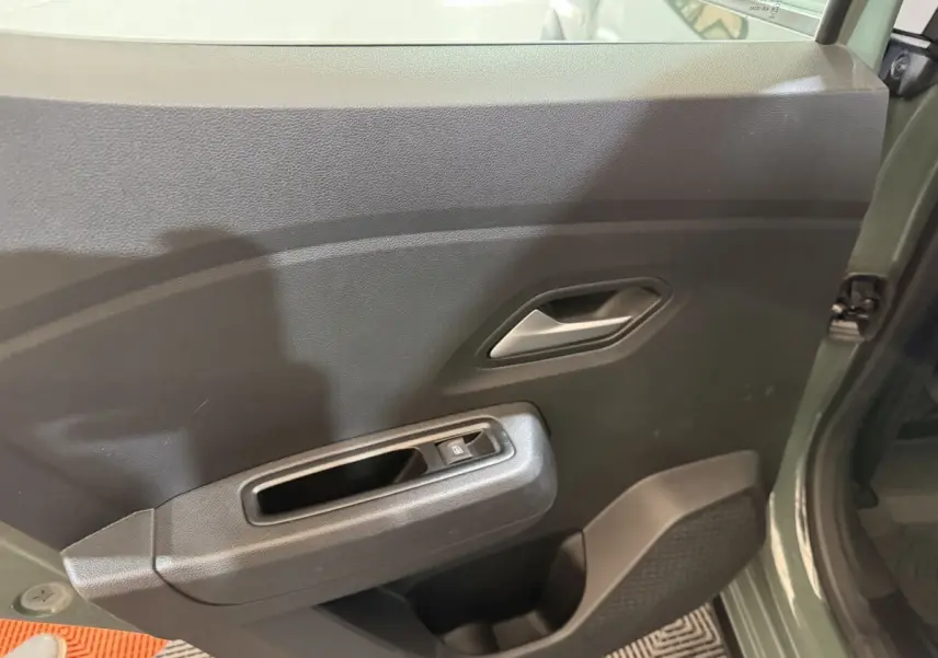 Vue intérieure côté gauche de la porte avant verte d'une Dacia Sandero Extreme+ avec commande de vitre électrique.