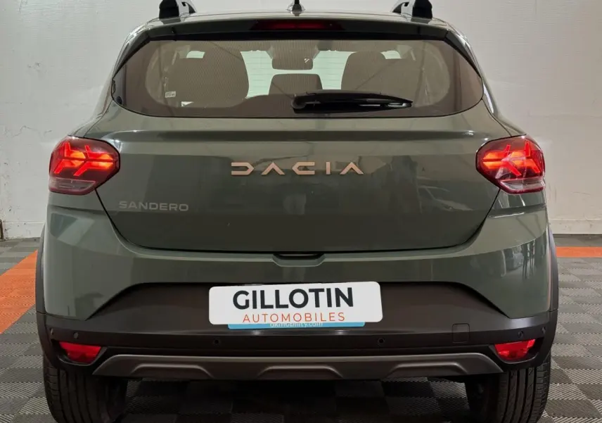 Vue arrière d'une Dacia Sandero Extreme+ TCe 110 2024 en vert avec feux LED allumés et barres de toit noires.