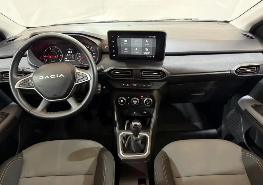 Vue intérieure avant de la Dacia Sandero 2024, volant multifonctions cuir, écran tactile central et levier de vitesse manuel.