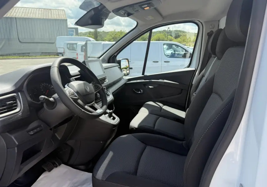 Intérieur vue côté conducteur du Renault Trafic blanc 2025, montrant le volant multifonctions et les sièges noirs.