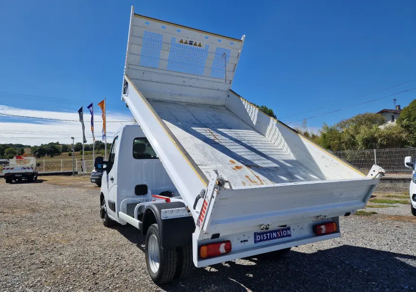 Renault Master Benne blanc vu en 3/4 arrière avec benne relevée et roues jumelées sur terrain extérieur.