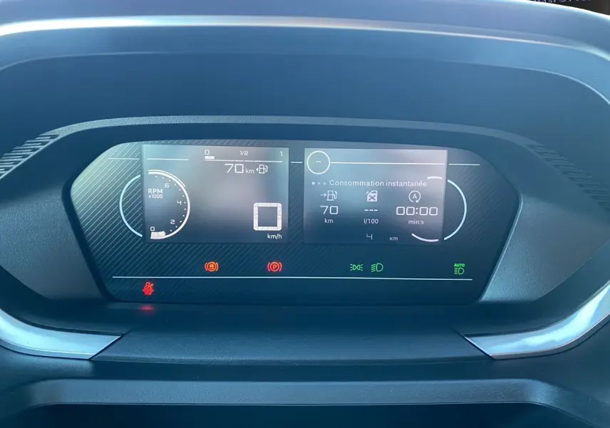 Tableau de bord numérique du Peugeot Partner 2024 affichant vitesse, consommation et compte-tours en vue frontale rapprochée.
