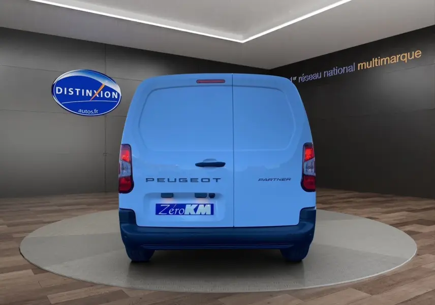 Vue arrière d'un utilitaire Peugeot Partner blanc avec portes battantes et logo distinctif sur fond showroom.