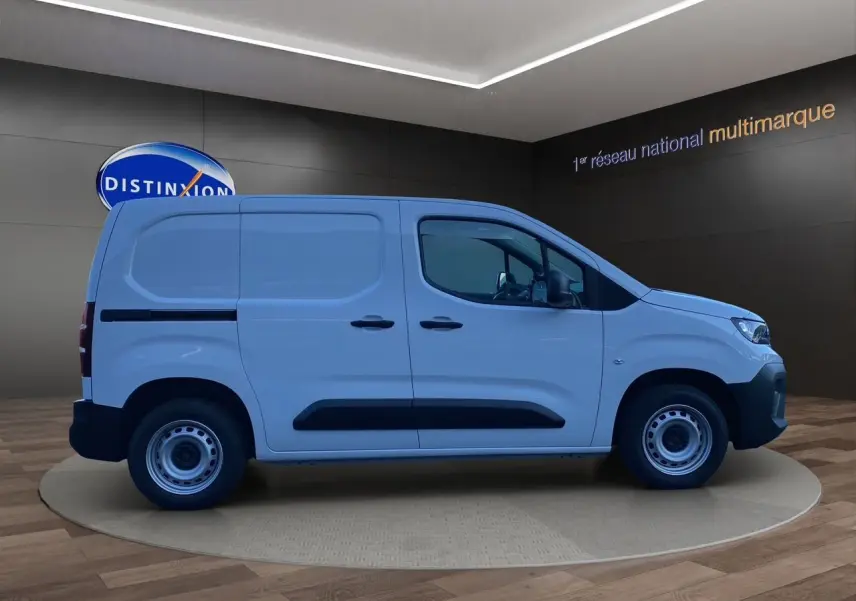 Vue latérale droite d'un utilitaire Peugeot Partner blanc avec protections noires et jantes acier en showroom.