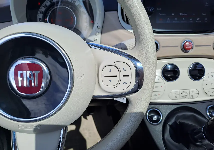 Vue rapprochée du volant beige et du tableau de bord clair d'une FIAT 500 blanche, version DolceVita 2022.