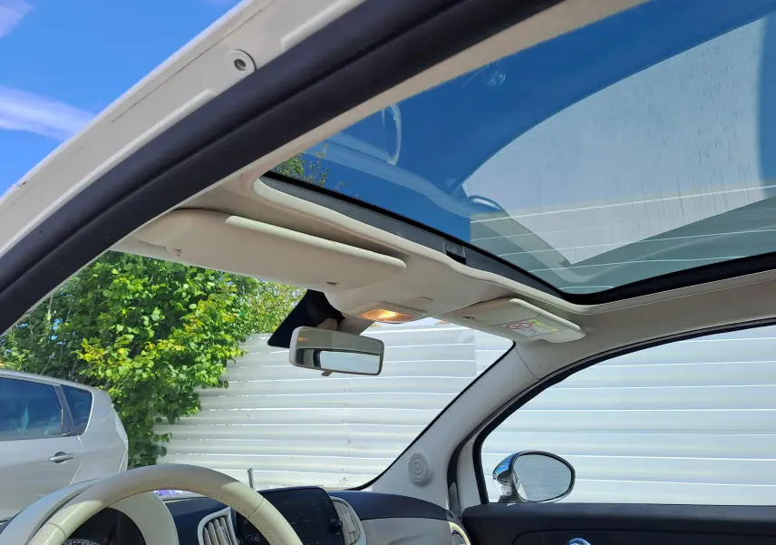 Vue intérieure avant de la FIAT 500 blanche 2022, toit panoramique ouvert et volant beige visible.