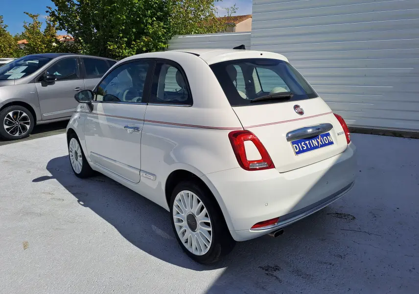 Fiat 500 blanche vue 3/4 arrière droit, avec jantes blanches et bande rouge décorative latérale.