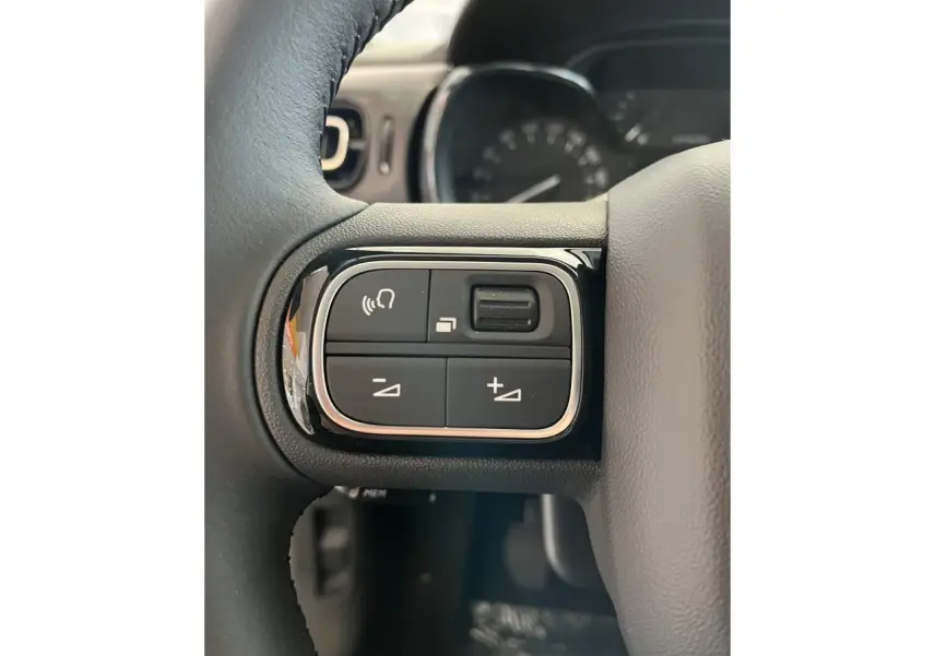 Gros plan sur les commandes audio au volant noir de la Citroën C3 blanche 2024, avec cadrans en arrière-plan flous.