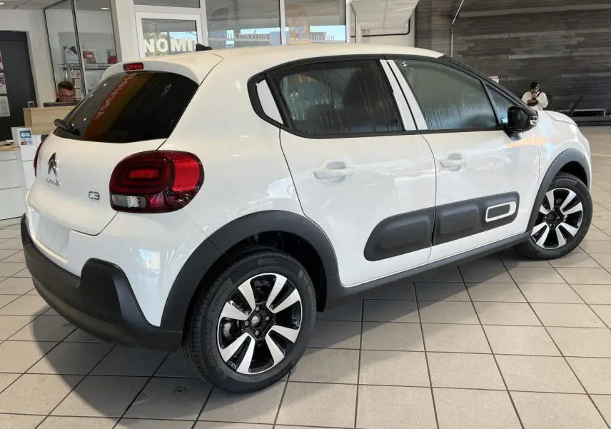 Vue 3/4 arrière droite d'une Citroën C3 blanche avec protections latérales noires et jantes alliage diamantées.
