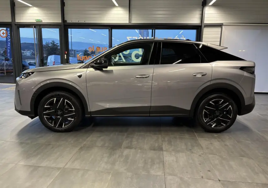 Profil droit d'un Peugeot 3008 GT hybride gris Artense avec toit noir en intérieur showroom.