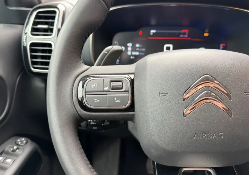 Gros plan sur le volant cuir multifonctions de la Citroën C5 Aircross 2025, avec commandes intégrées et logo chromé.
