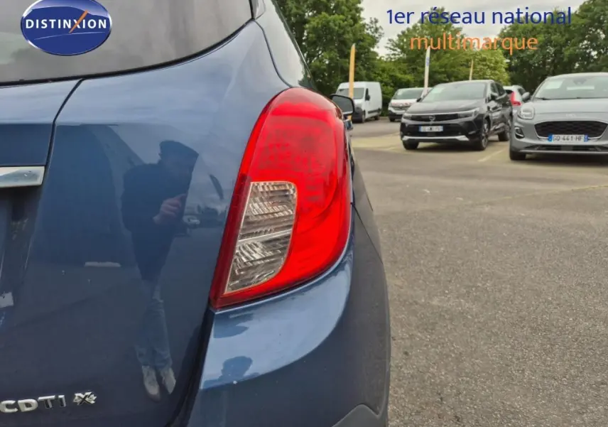 Gros plan sur le feu arrière droit d’un Opel Mokka bleu outremer, avec partie arrière et parking en arrière-plan.
