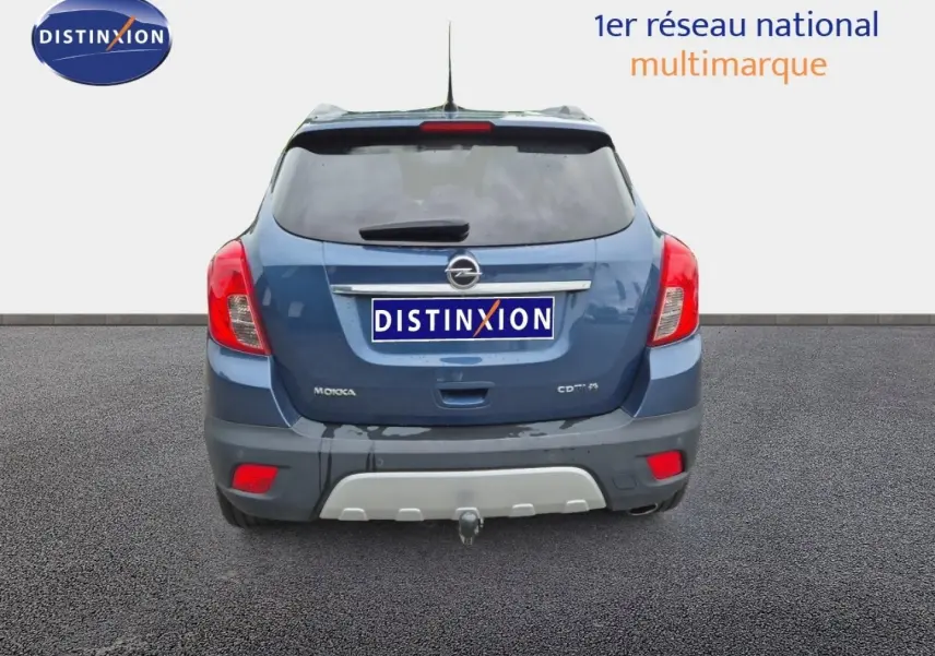 Vue arrière d'un Opel Mokka bleu outremer avec attelage et feux arrière rouges visibles sur fond neutre.