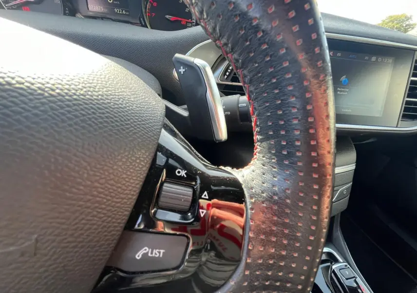 Gros plan sur le volant cuir noir à surpiqûres rouges de la Peugeot 308 SW GT Line avec commandes intégrées et écran tactile visible.