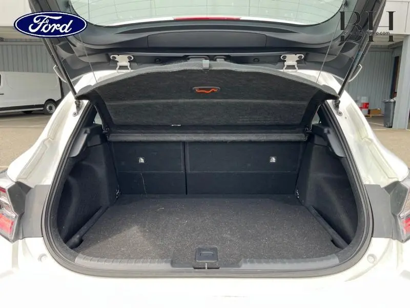 Coffre ouvert vu de l'arrière d'une Toyota Corolla blanche Pure 2022, avec intérieur de coffre noir et cache-bagages relevé.