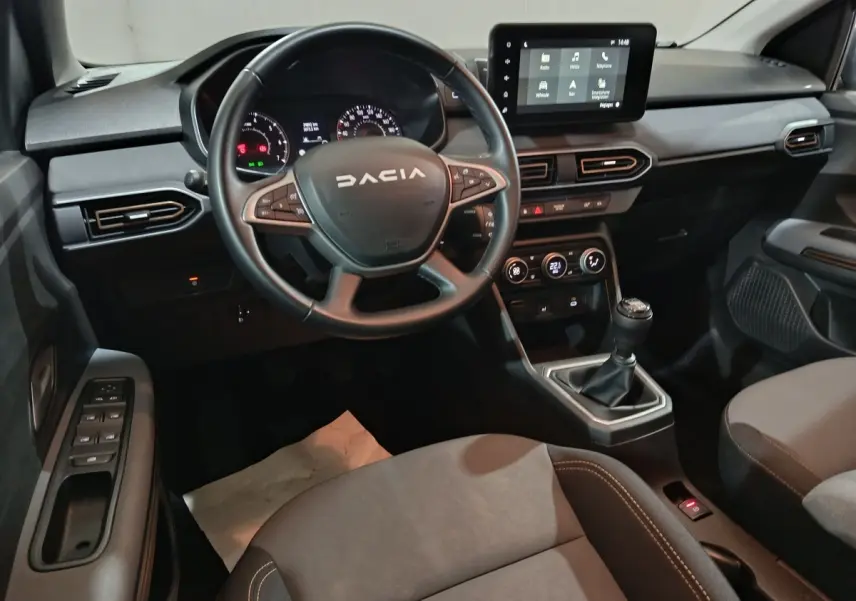 Vue intérieure avant de la Dacia Sandero 2024, tableau de bord noir avec écran tactile et volant multifonctions en cuir.