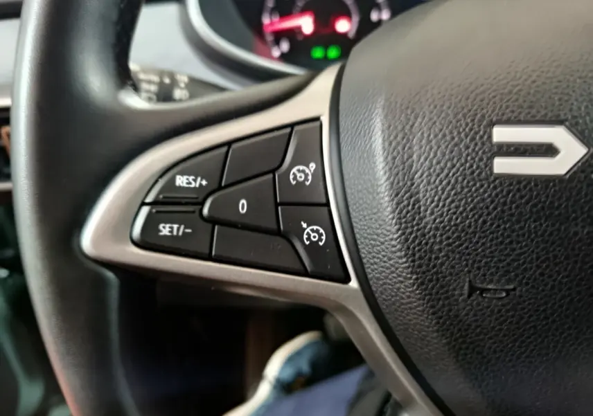 Gros plan sur les commandes de régulateur de vitesse à gauche du volant noir de la Dacia Sandero Extreme+ TCe 110 2024.