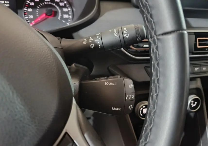 Gros plan sur la commande multifonction noire à gauche du volant cuir noir dans l'habitacle de la Dacia Sandero verte 2024.