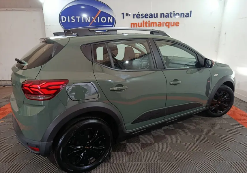 Vue 3/4 arrière droite d'une Dacia Sandero Extreme+ 2024 verte avec jantes noires et rails de toit assortis.