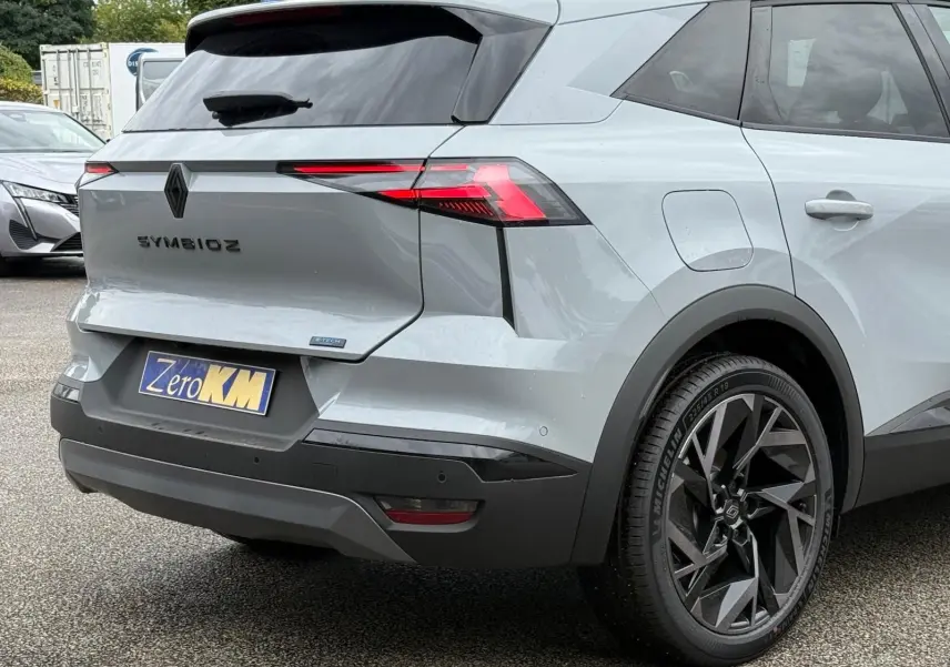 Vue 3/4 arrière droite du Renault Symbioz gris Rafale, mettant en valeur ses feux LED et ses jantes noires au design géométrique.