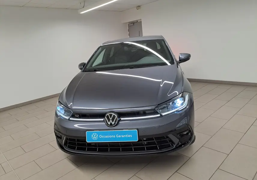 Vue avant d'une Volkswagen Polo 1.0 TSI R-Line gris cendré avec phares allumés dans un showroom.