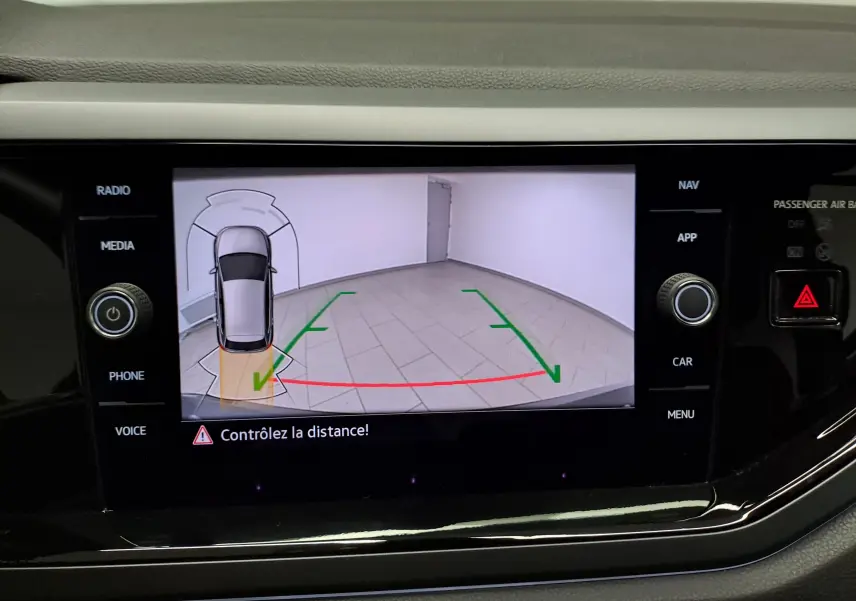 Écran de caméra de recul affichant une Volkswagen Polo gris cendré en vue aérienne avec guidage de trajectoire verte et rouge.