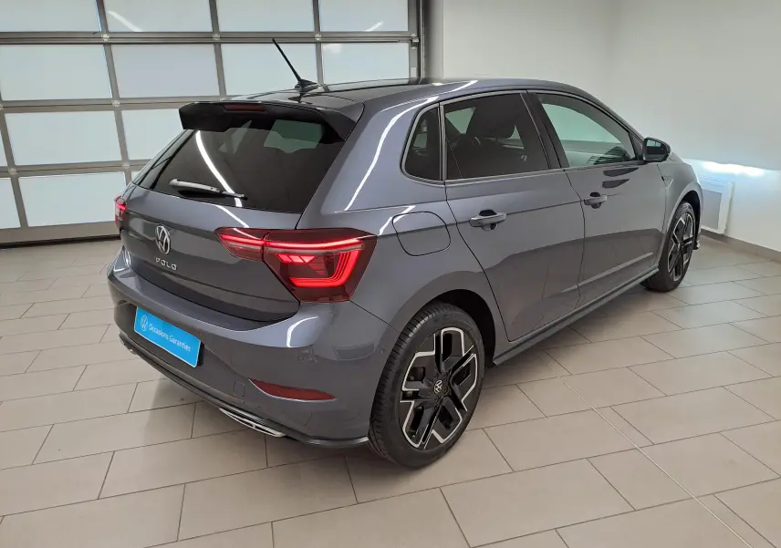 Vue 3/4 arrière droite d'une Volkswagen Polo 1.0 TSI R-Line gris cendré métallisé avec jantes noires et feux LED allumés.