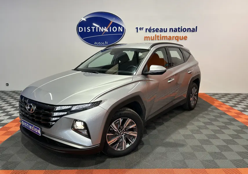 Vue 3/4 avant d'un Hyundai Tucson gris Shimmering Metal avec feux allumés dans un showroom.