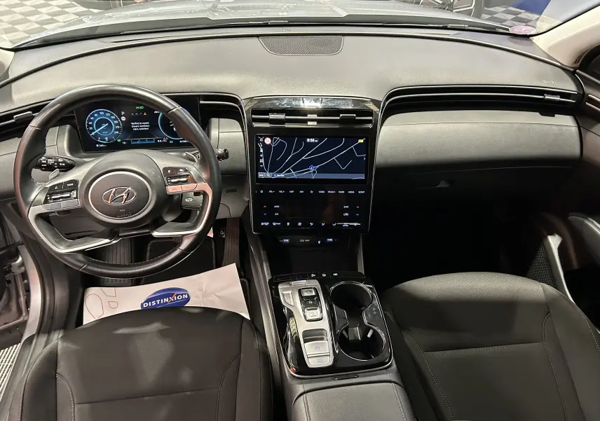 Vue intérieure du tableau de bord et volant cuir noir d’un Hyundai Tucson Hybrid 2022 avec écran tactile GPS central.