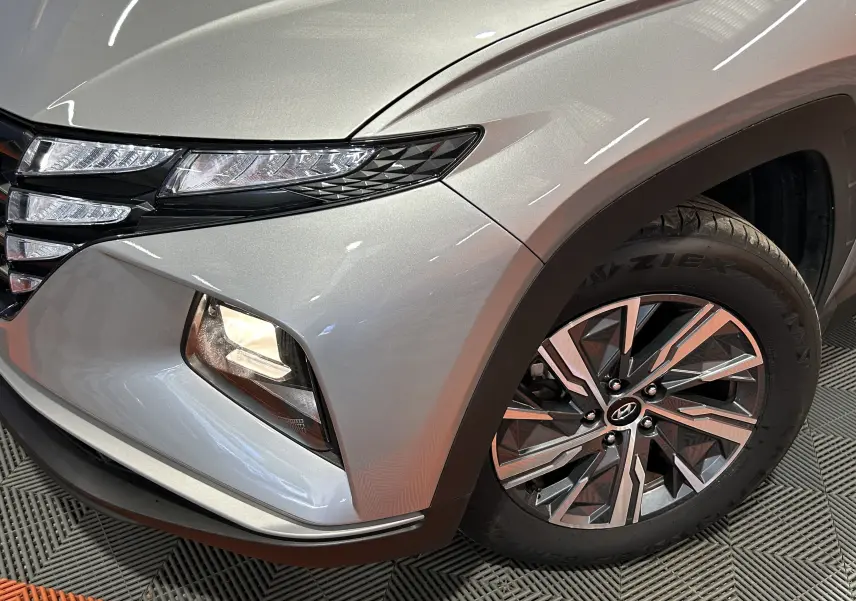 Gros plan sur l’avant droit gris Shimmering Metal du Hyundai Tucson Hybrid, mettant en valeur le phare et la roue alliage.