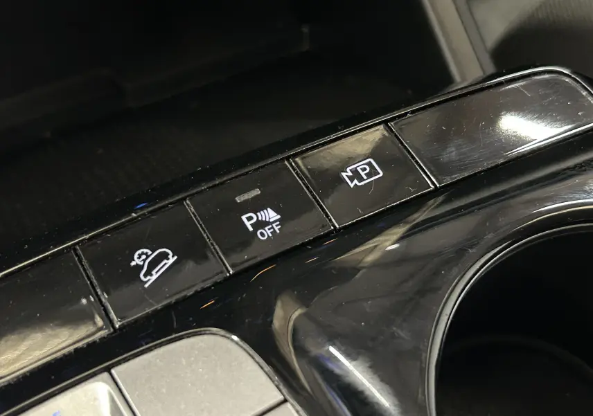 Gros plan sur les boutons de commande du système d’aide au stationnement et caméra dans l’habitacle noir du Hyundai Tucson gris.