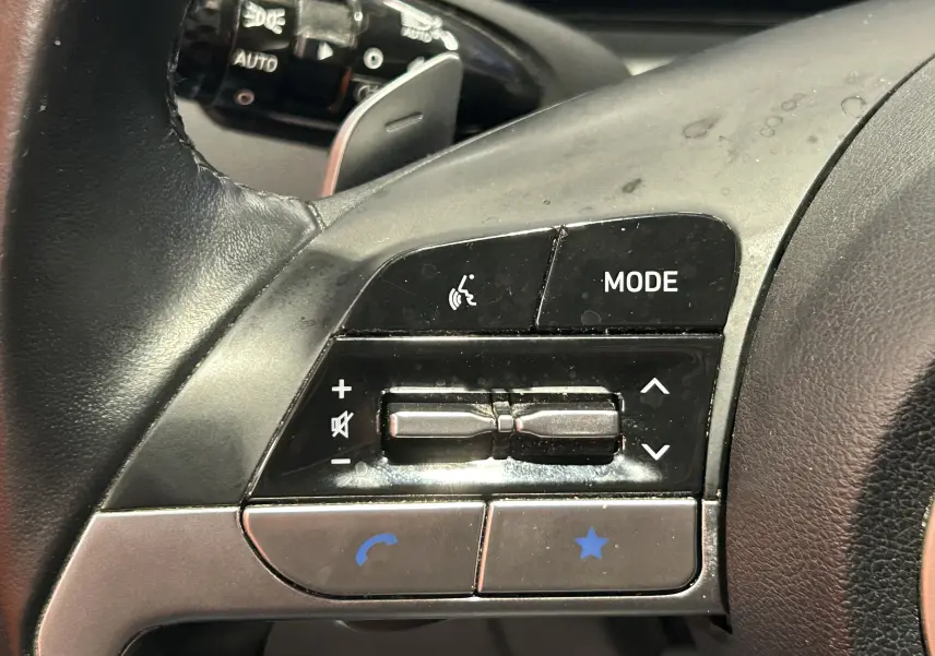 Gros plan sur les commandes multifonctions à gauche du volant en cuir noir du Hyundai Tucson hybride 2022.