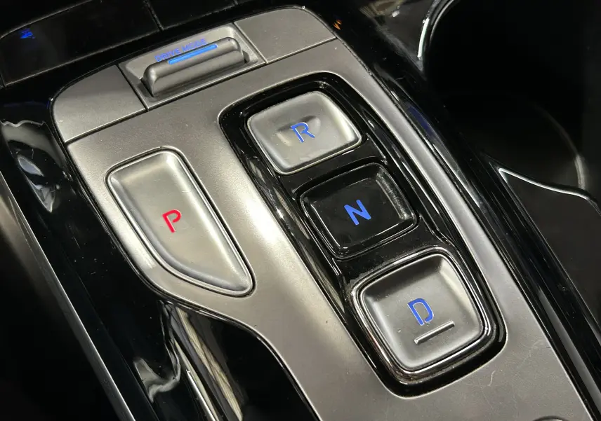 Gros plan sur la console centrale du Hyundai Tucson gris, montrant les boutons de la boîte automatique avec éclairage bleu et rouge.