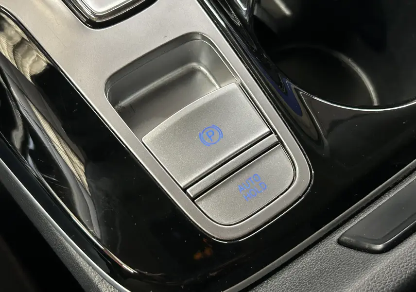Gros plan sur la commande de frein à main électronique et bouton Auto Hold dans l’habitacle noir du Hyundai Tucson Hybrid 2022.